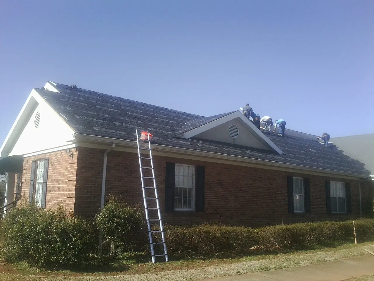 Crew tearing shingles off a brick ranch roof with a ladder set — Emergency Roof Repair work by our crew in Bourneville