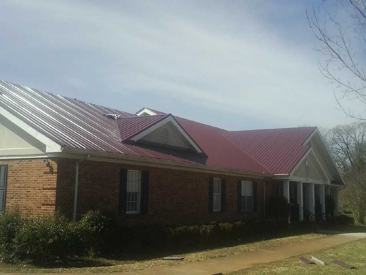 Red metal roof with gabled entries on a long brick building, from a Hail Damage Roof Repair job in Bourneville