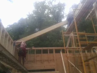 Carpenter raising a rafter beam on a new second story frame in Bourneville