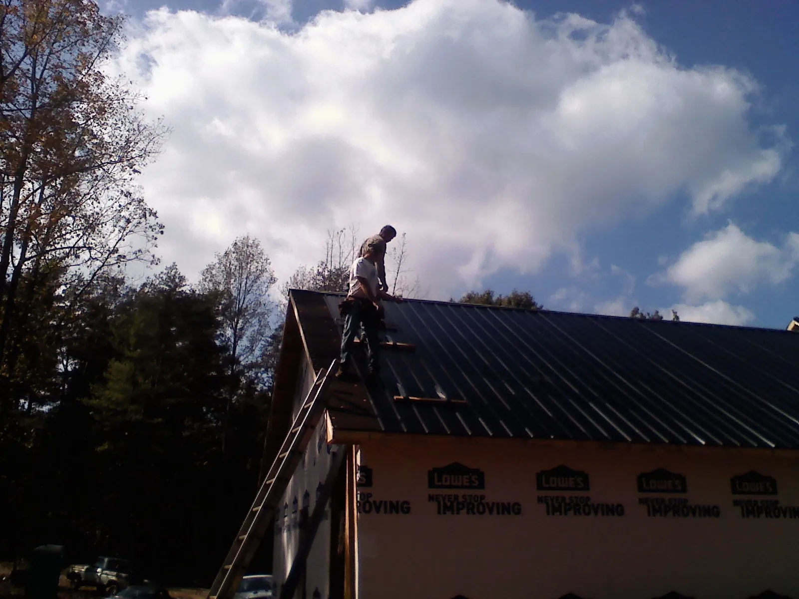 Roofer fastening dark metal panels high against a cloudy sky, from a Roof Inspection job in Bourneville