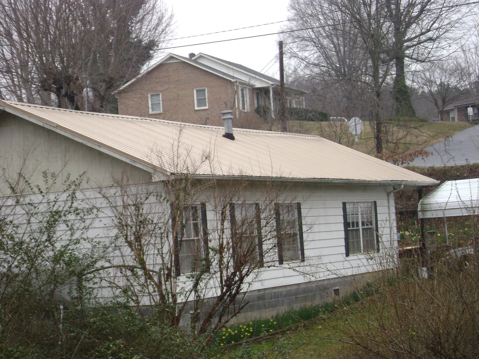 Tan metal roof on a white sided house set into a hillside — Commercial Roofing by Roofing Brothers in Bourneville