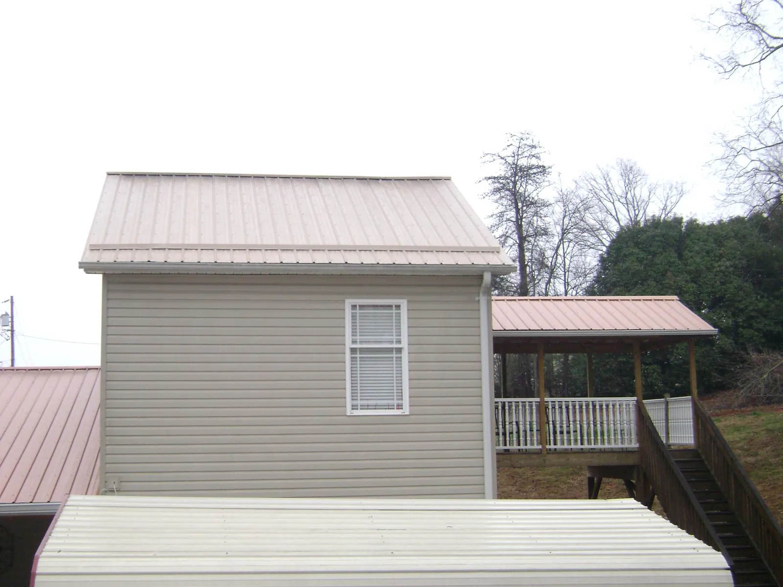 Tan metal roofs on a two story addition and attached porch, from a Roof Replacement job in Bourneville